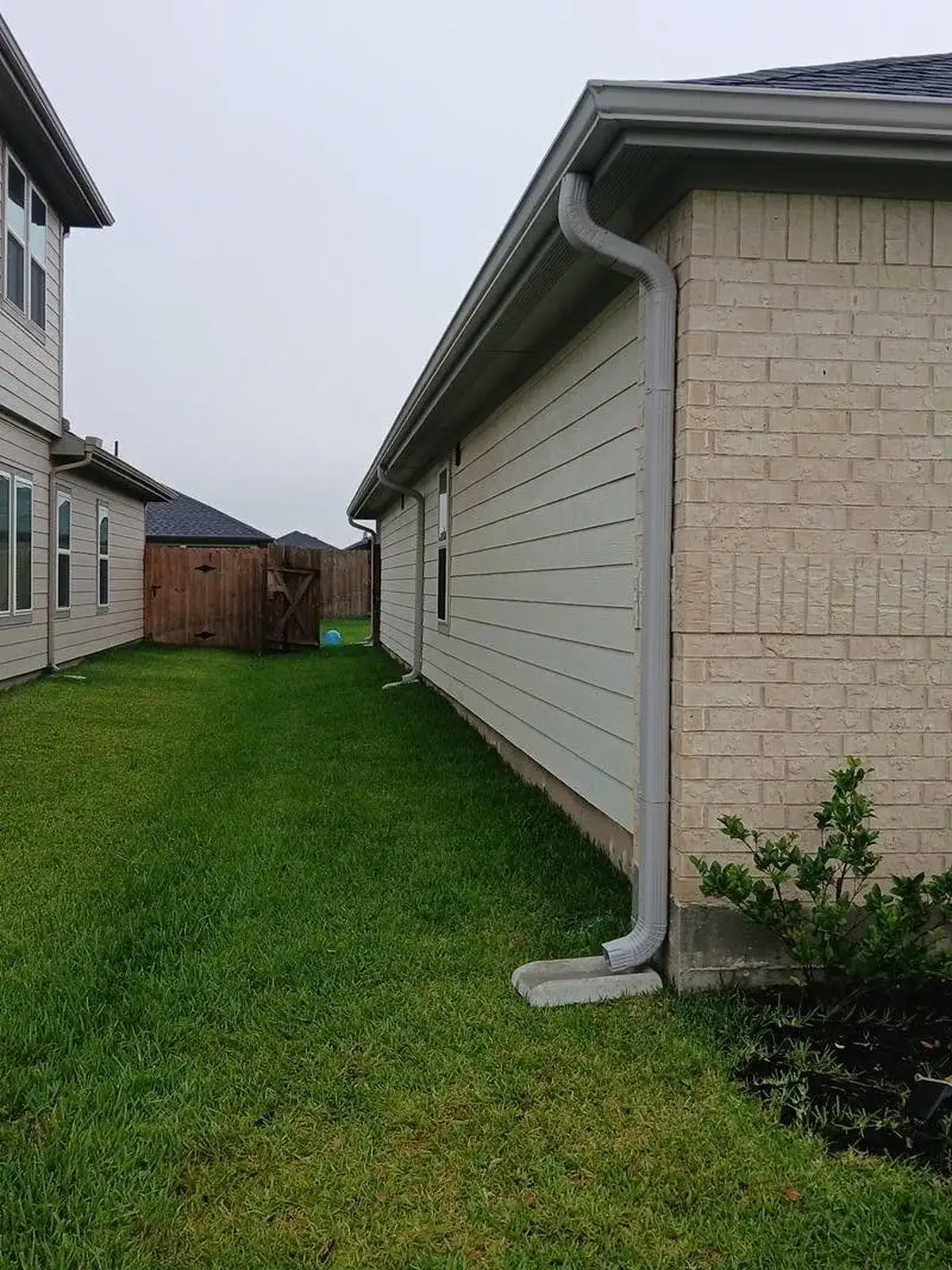 Gray downspout installation at the corner of a house in Houston